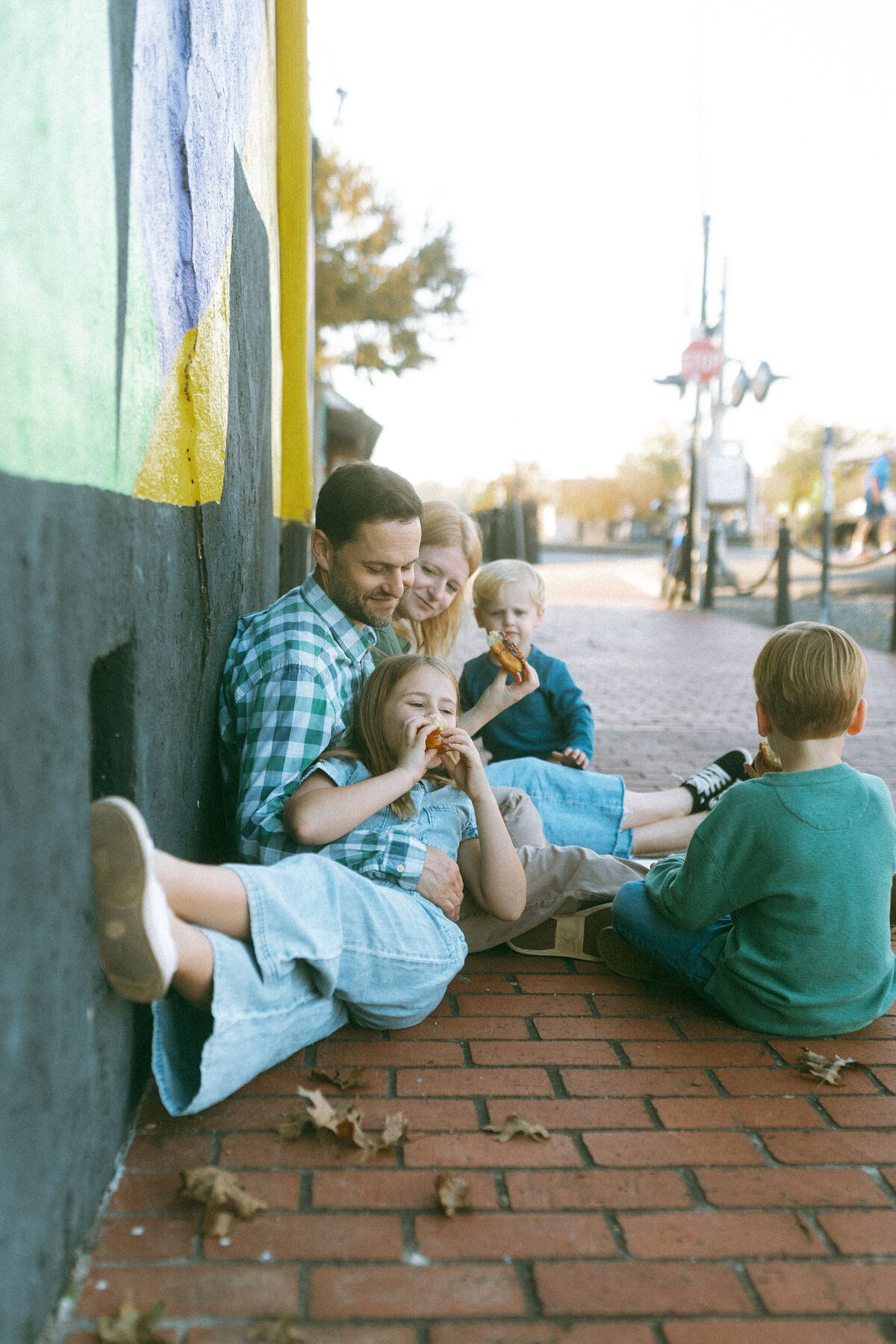 A family sitting on a sidewalk in downtown Marietta, ga eating donuts together. 
