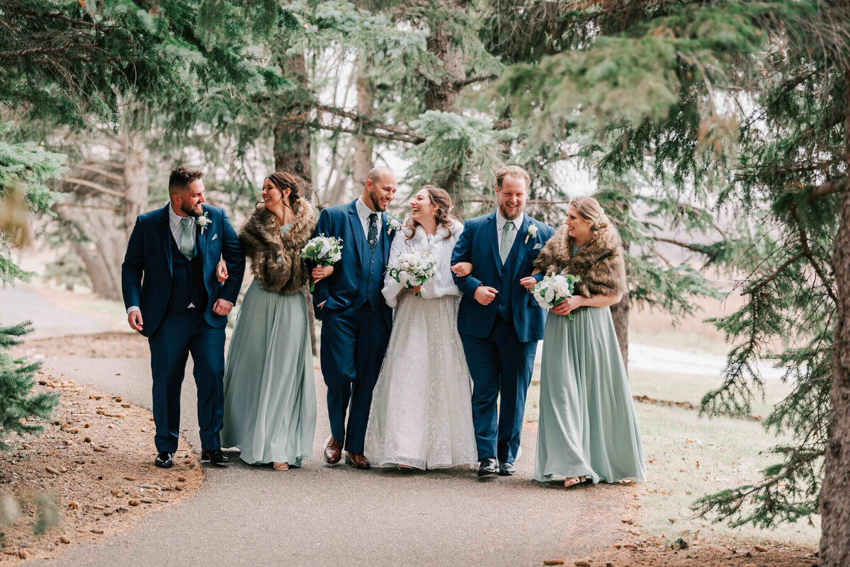Bride, groom and wedding party stand boy, girl and arms linked. Walking towards camera. 