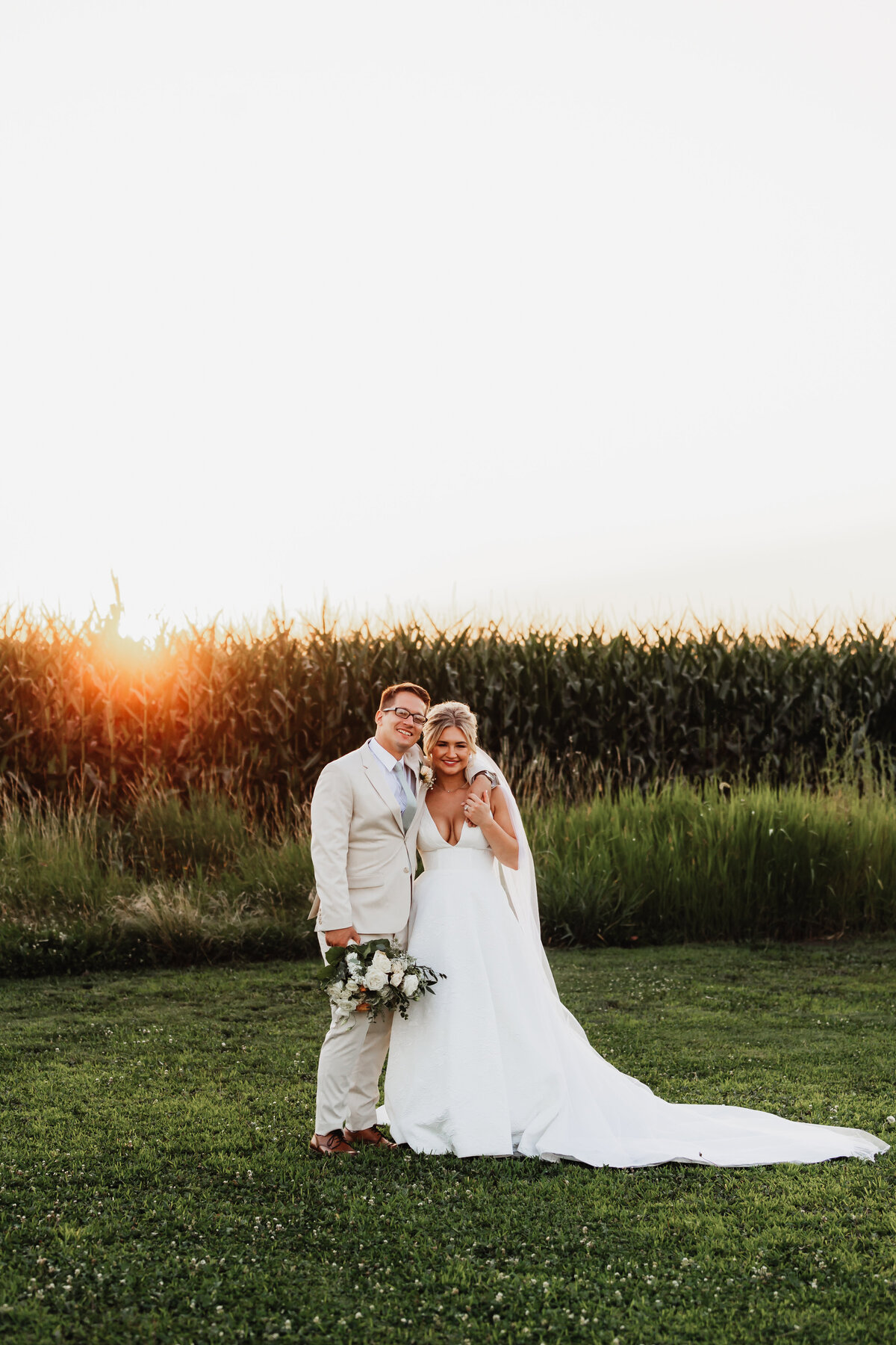 A couples portrait on their wedding day in front of a corn field.