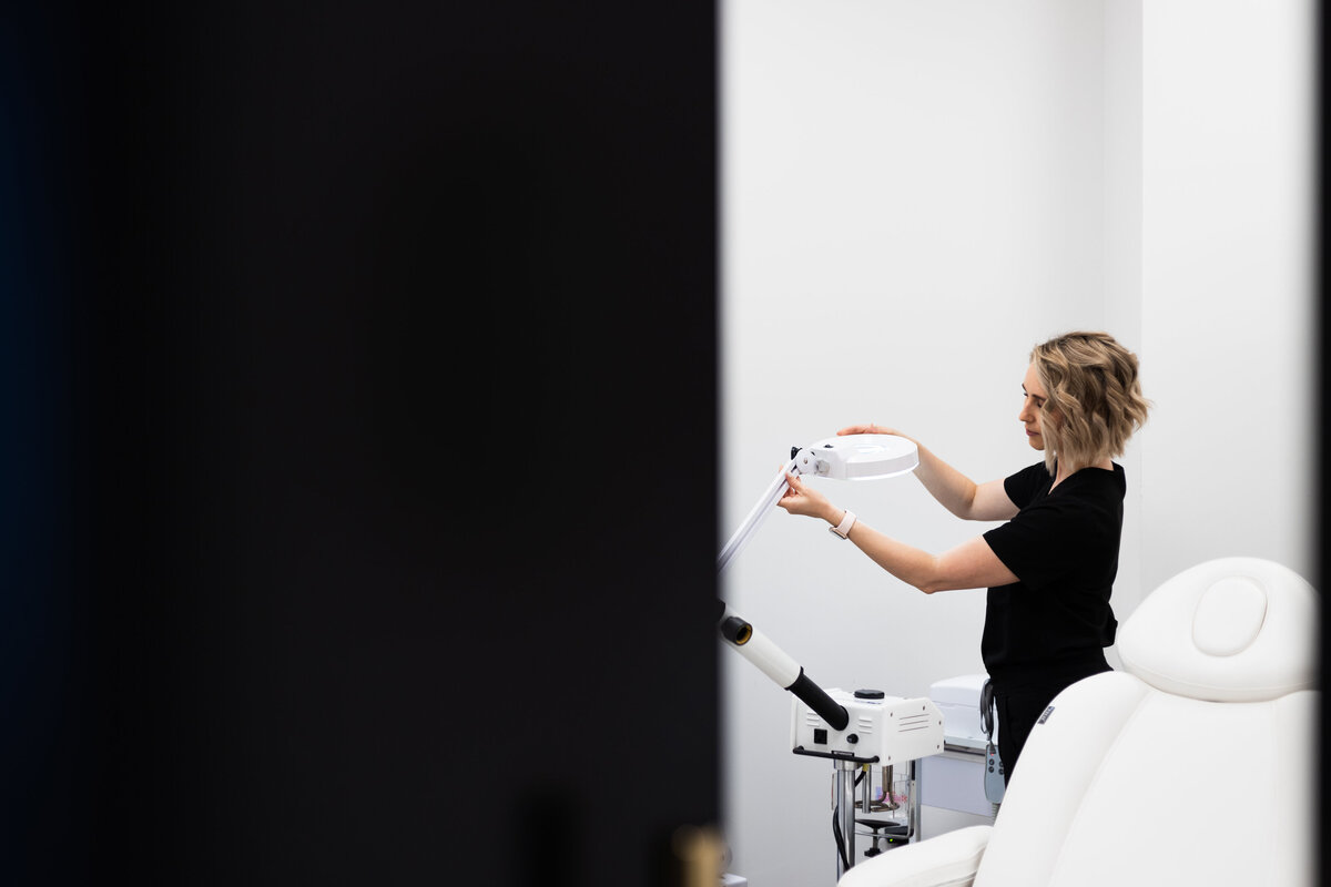 Esthetician in salon adjusting the ringlight next to client chair