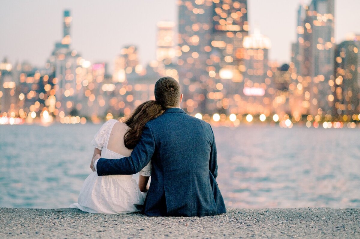 an engaged couple sitting with their arms around each other with the lit up Chicago cityscape in the background