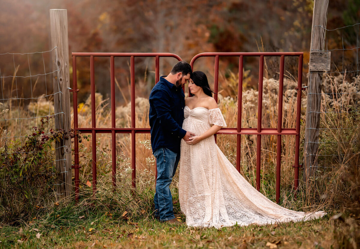 A couple stands in front a red gate and touches foreheads during their portrait session with an  Asheville Maternity Photographer