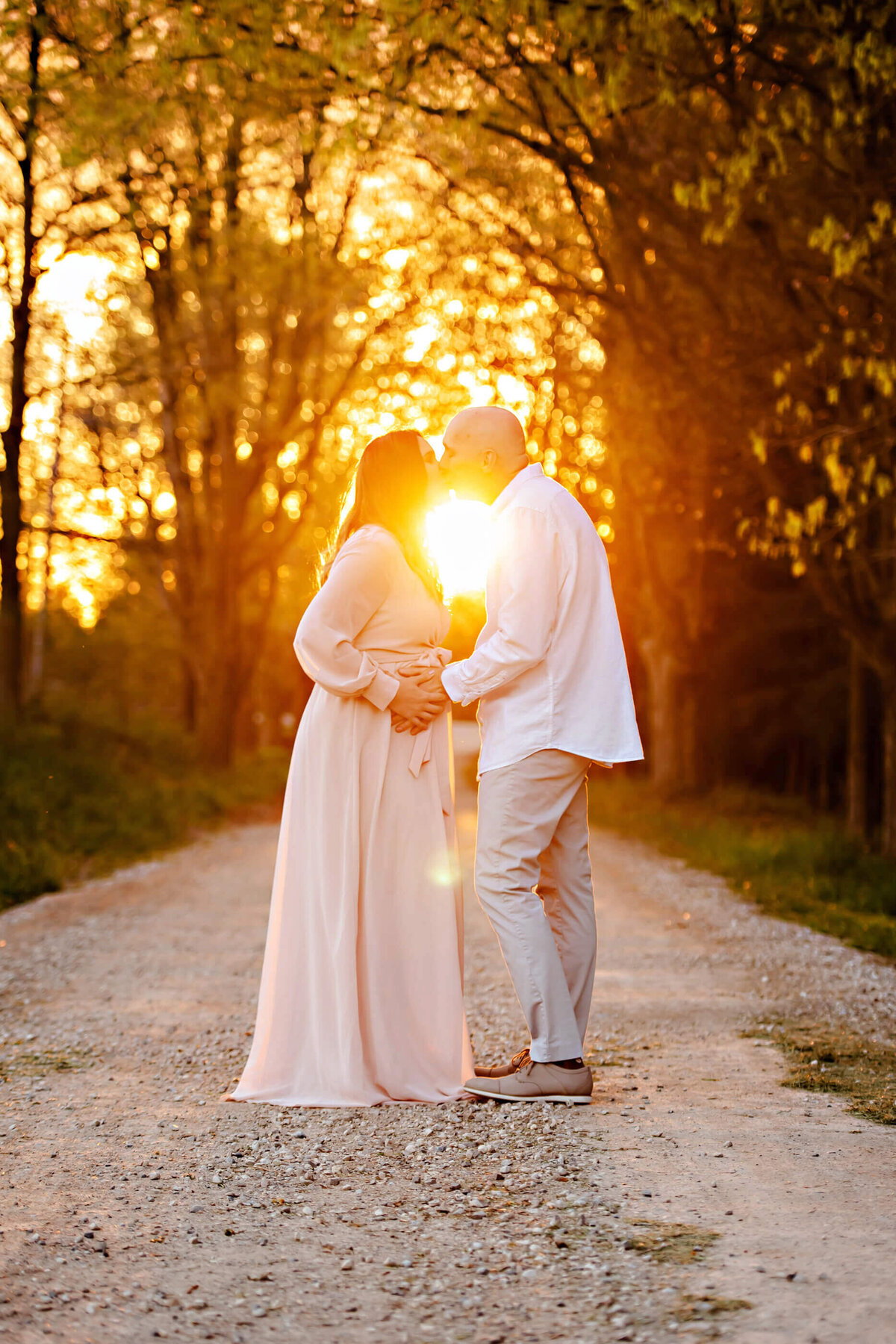 husband and wife standing in a dirt road with the golden sunlight behind them for her outdoor maternity photos in Burlington, ON