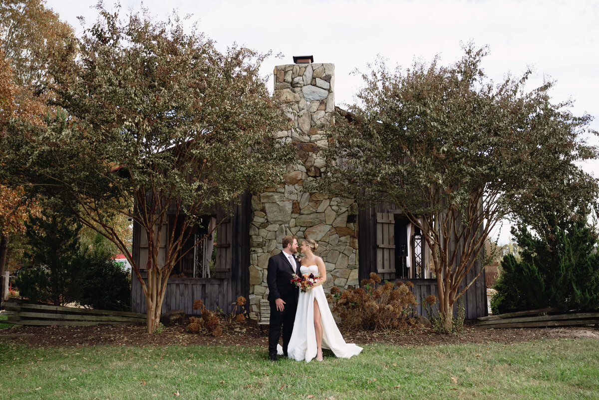 Charlottesville wedding venues outdoor space with bride in a satin gown leaning into her groom as they stand together in front of a stone building with large crepe murdles surrounding the building