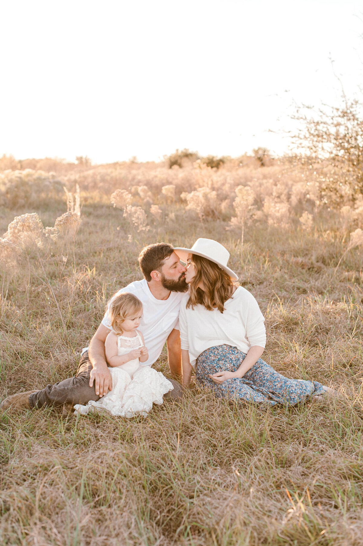 Orlando Maternity Photographer captures a kiss at sunset of soon to be parents sitting in a tall grass field.