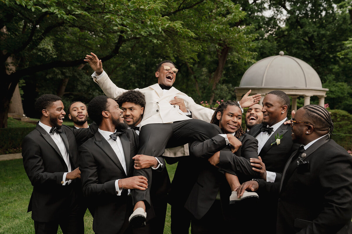 black wedding party lifts and carries groom