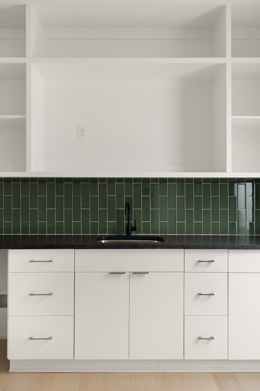 green glass tile backsplash in kitchenette with white cabinetry and black countertops