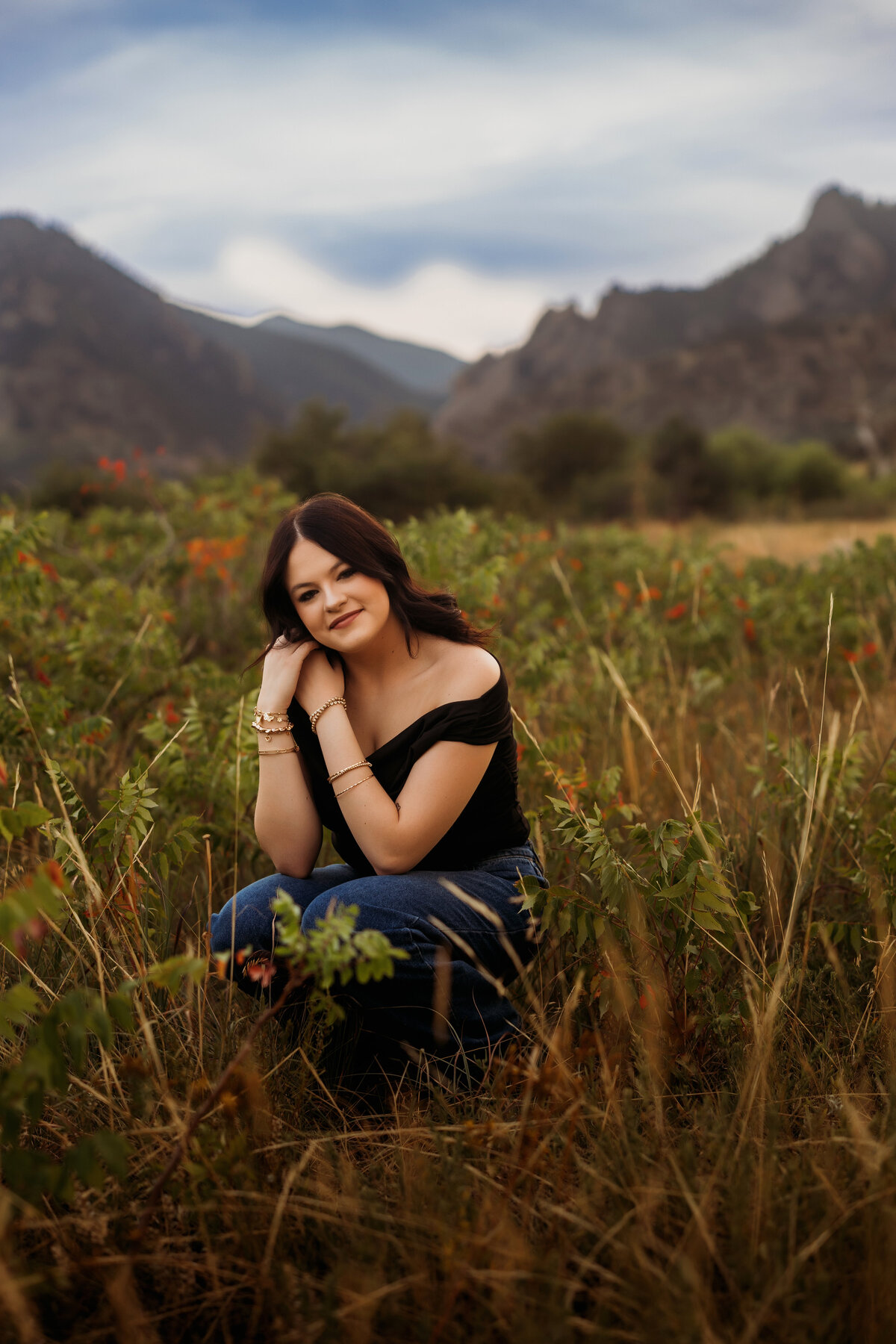 Senior girl stands in the middle of tall grasses and nature with mountains in the background for her senior photos just outside of Denver