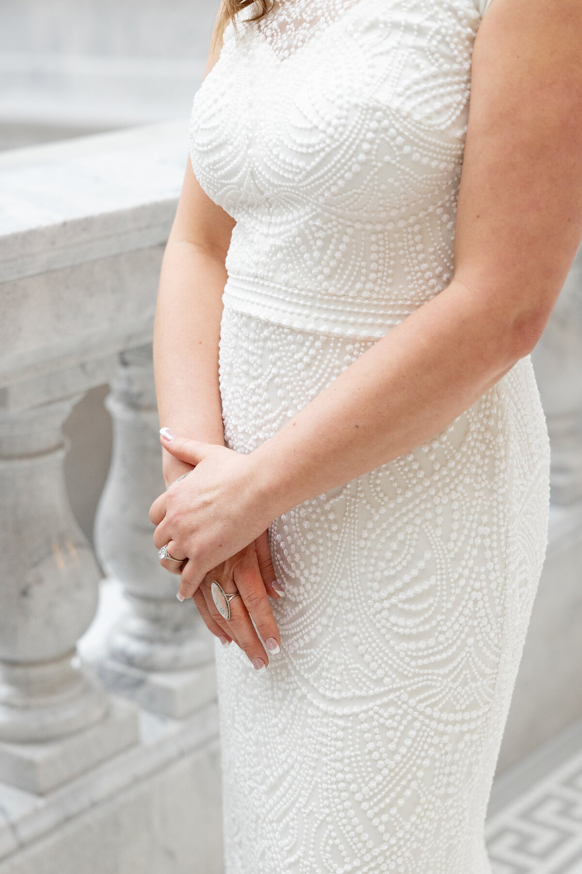 Close-up shot of the intricate beaded details on the bride’s wedding dress as she gracefully clasps her hands.