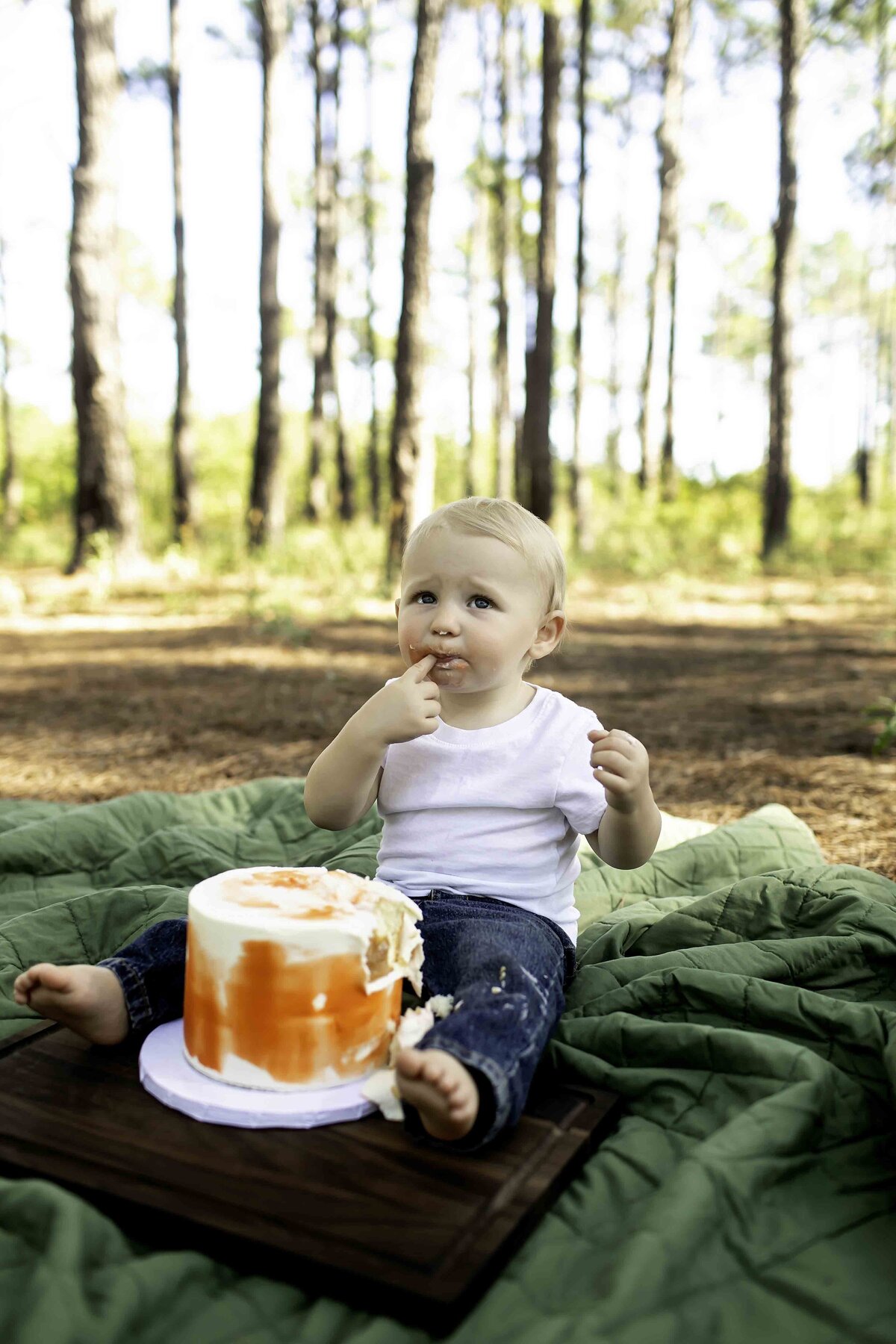 Birthday boy in suspenders and overalls, laughing as he smashes his birthday cake, surrounded by tall pine trees
