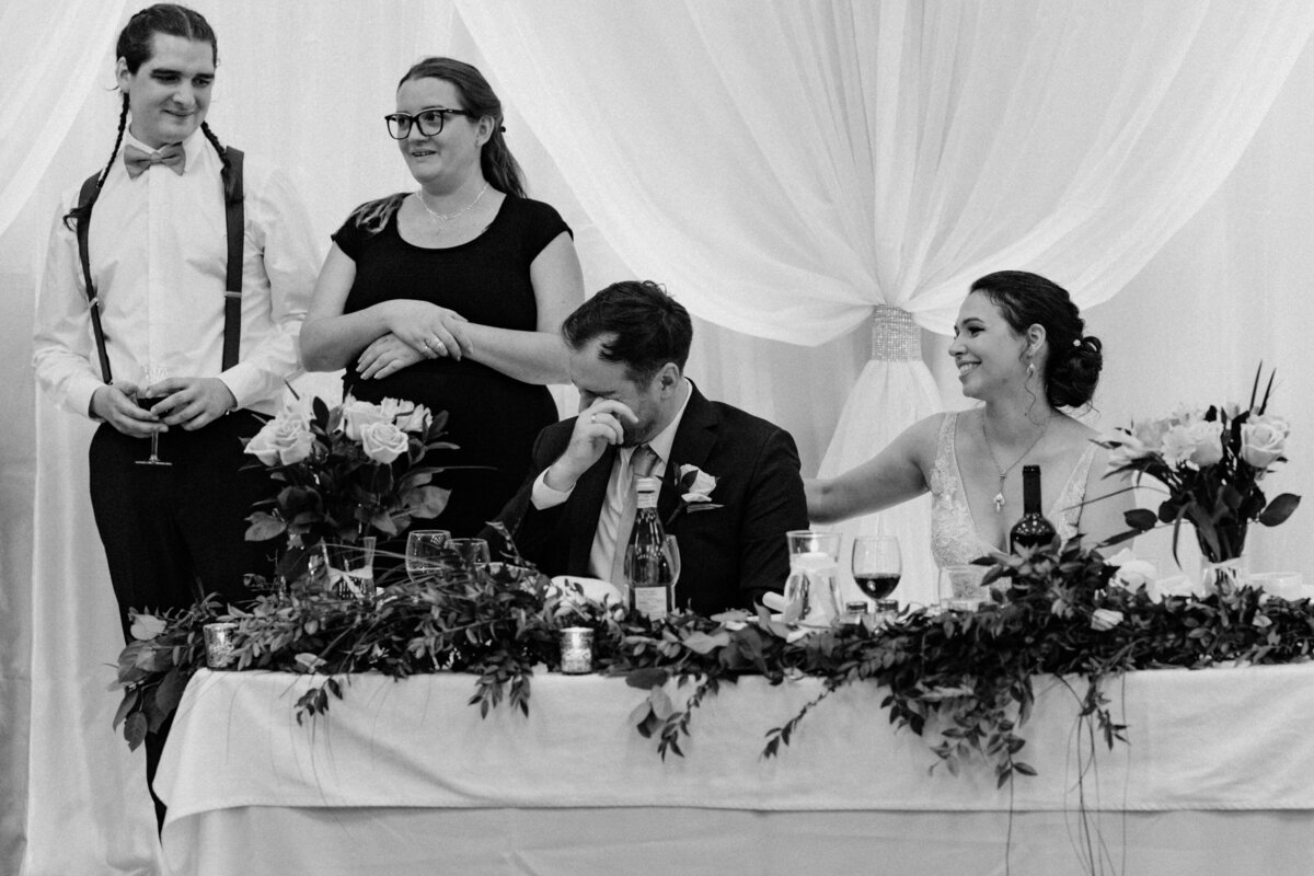 The groom wiping his tears at the touching speech as the bride consoles him with a smile