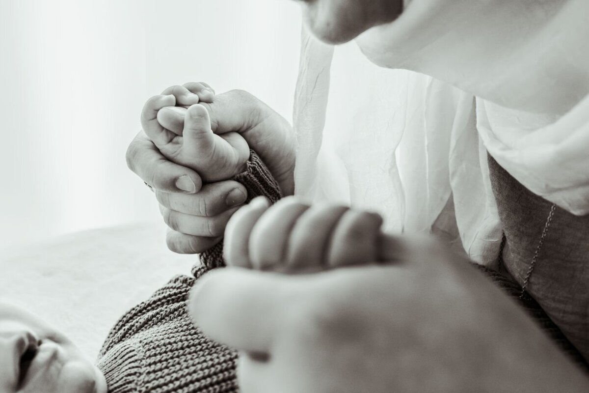 A tender monochrome close-up of a mother gently holding the tiny hands of her newborn baby