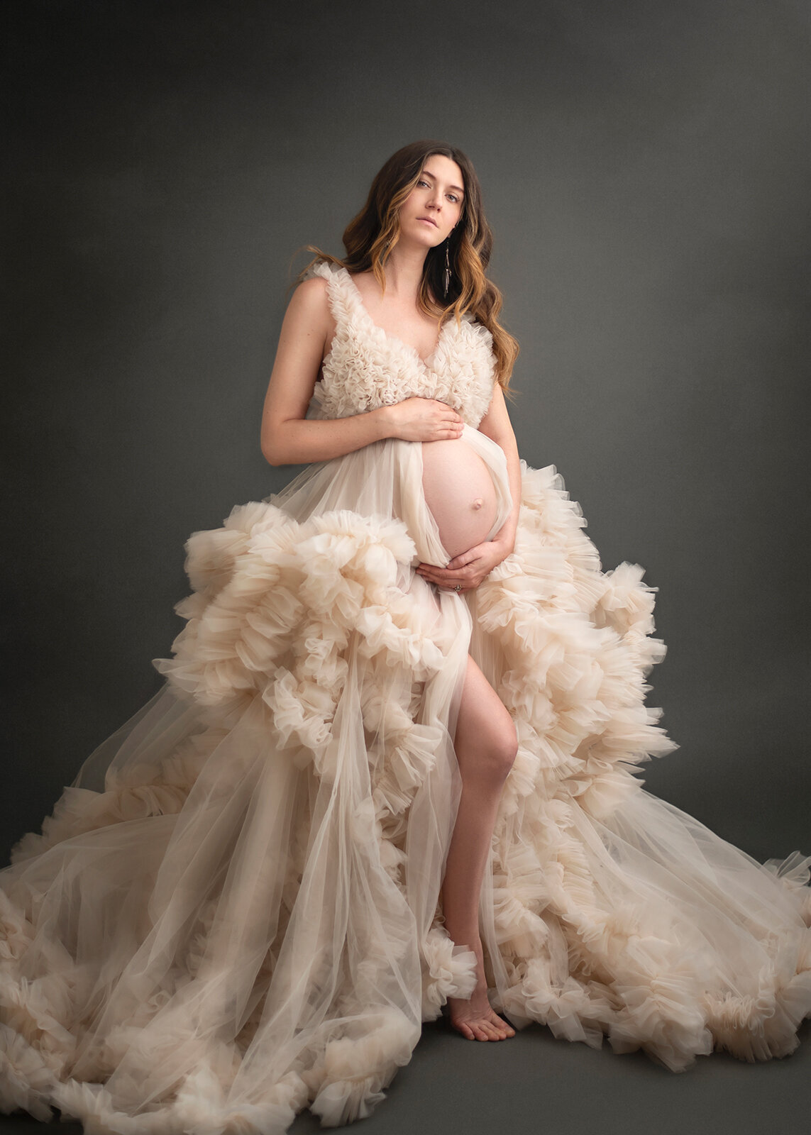 mom in white tulle gown looking at camera and holding her pregnant belly at her photoshoot in St. Louis