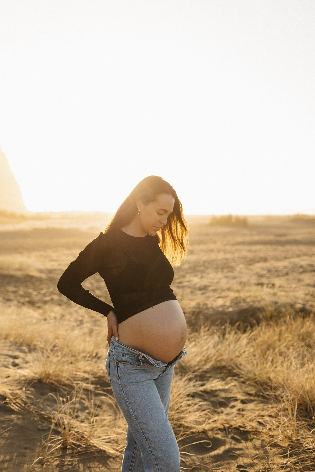 A mother to be wears a black top and a pair of jeans during a sunset maternity photoshoot with christchurch photographer lucy jane