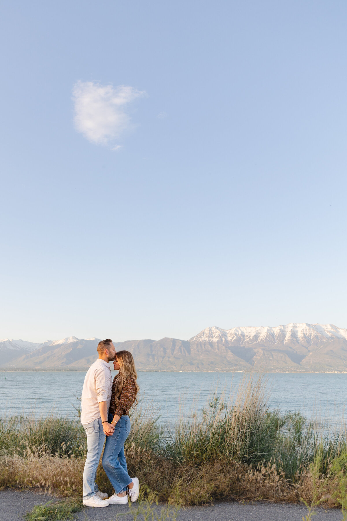 A man kisses his fiancée’s forehead as they stand hand in hand. Taken by Cassie Lee Photography