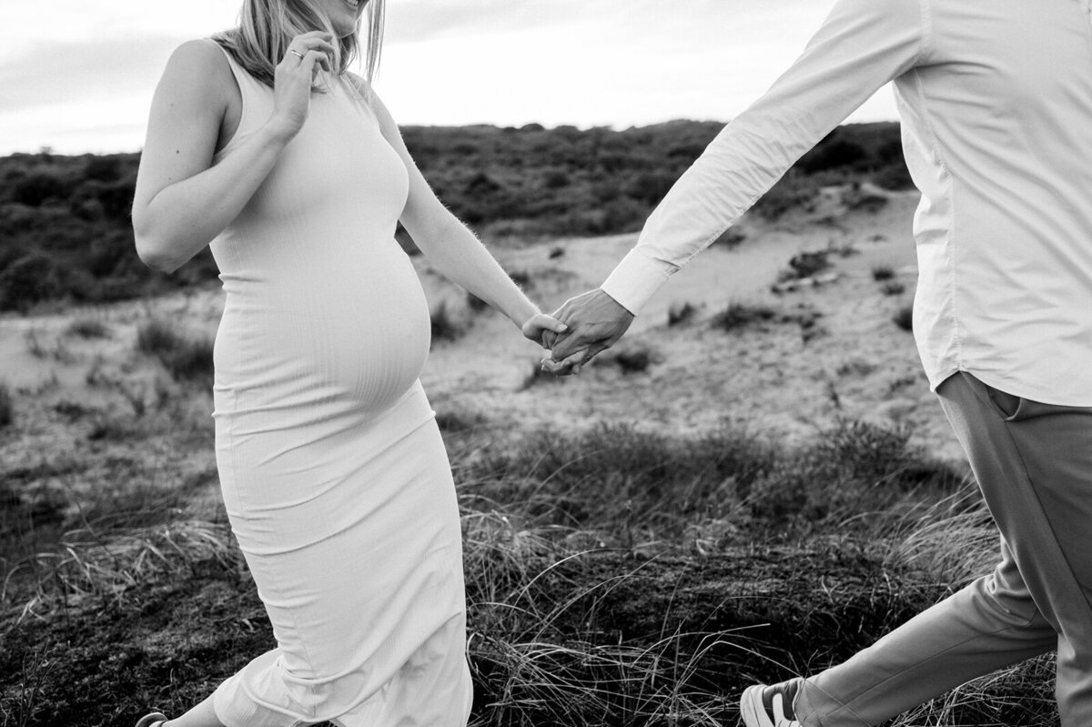 Zwanger koppel loopt hand in hand door de duinen