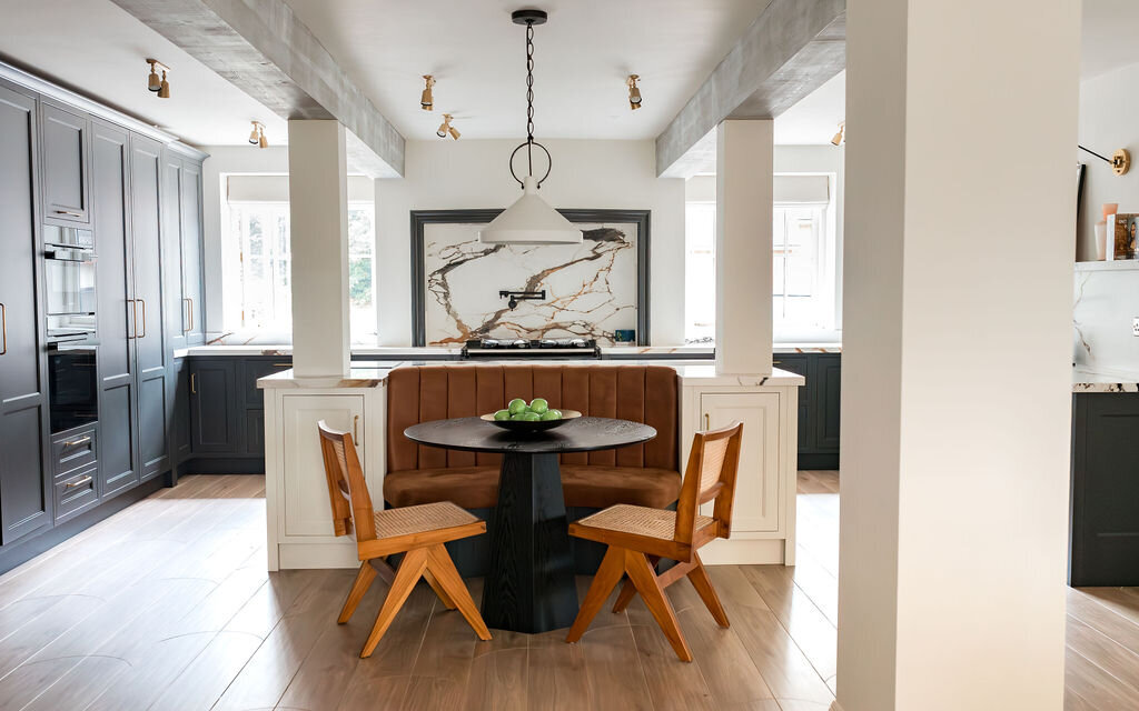 Modern kitchen with black cabinets, light wooden floor, and a central island. The kitchen has a built-in seating area with two wooden chairs and a small table.