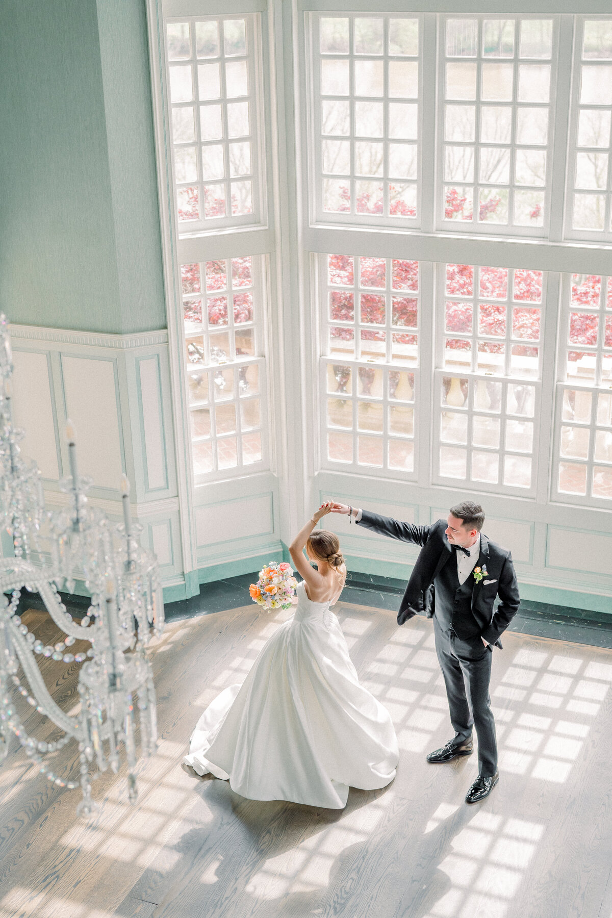 Groom twirling the bride in the stunning light blue ballroom with floor to ceiling windows