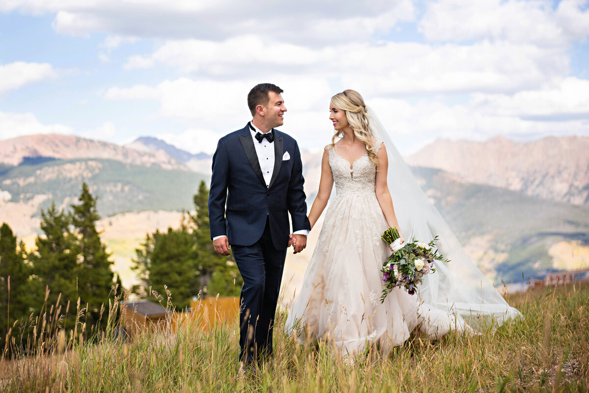 bride & groom walk hand in hand with vail mountains behind