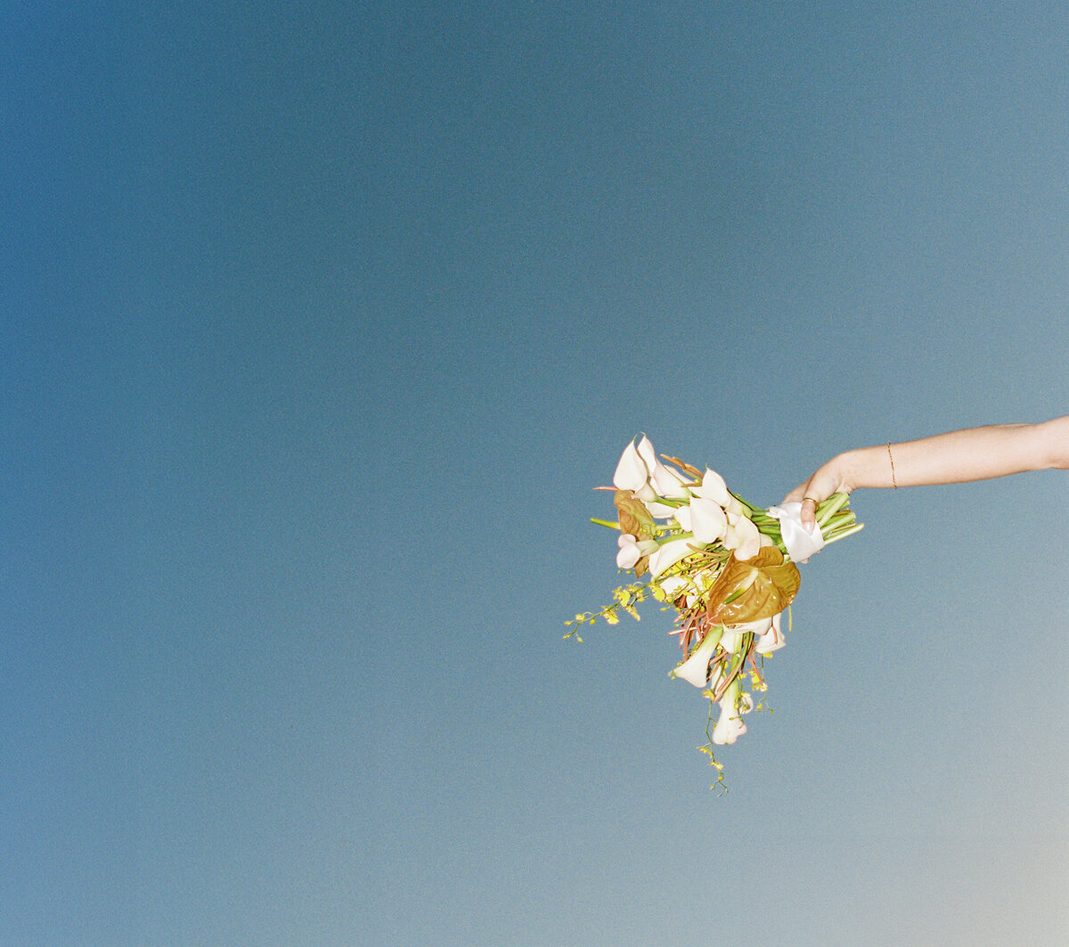 Bride holding bouquet against sky backdrop, captured on film with flash | Editorial wedding portrait by Tess Gearhart Photography