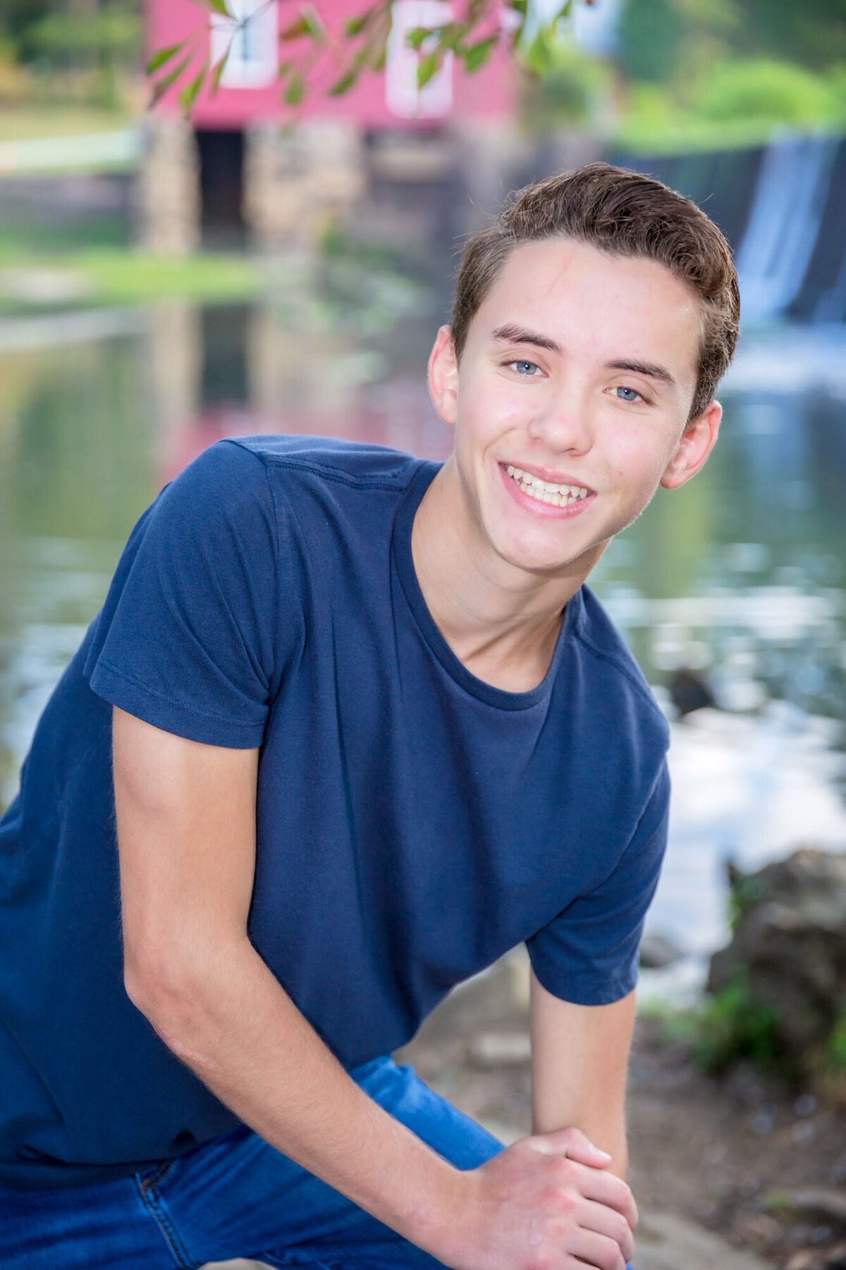 Proud senior posing in front of a waterfall and red barn at Starr's Mill pond in Fayetteville Georgia.