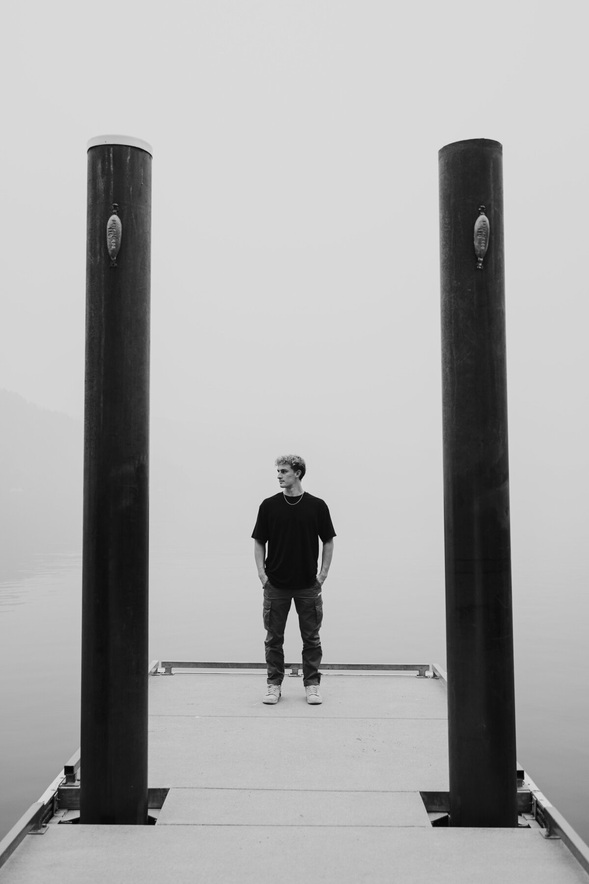 Black and white shot of young man standing at the end of dock with no horizon visible.