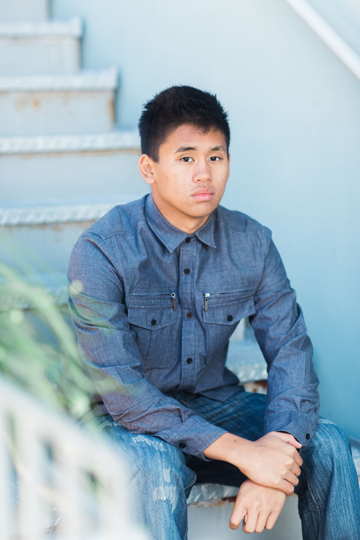 Senior portraits taken of boy in blue shirt against blue stairs in Daybreak, Utah.