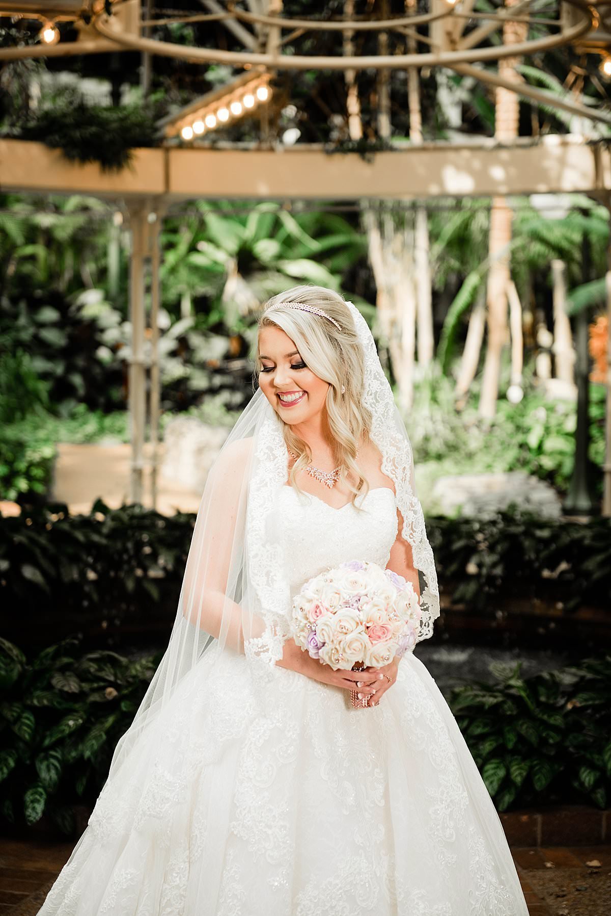 Bride wearing Cinderella  ballgown and smiling to the side, lace trim veil and holding light colored bouquet