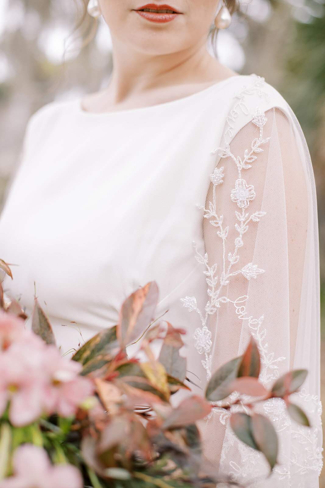 The beaded bridal capelet on the Dolores wedding dress style is custom embroidered with a flower and love motif.