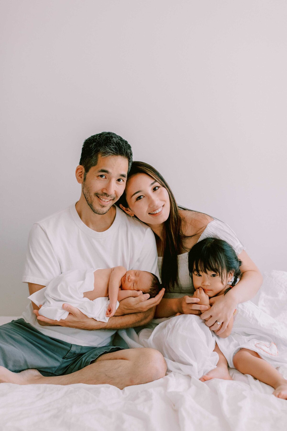 family of 4 with their toddler daughter and newborn baby boy. mom resting head on dad's shoulder and snuggling her babies.
