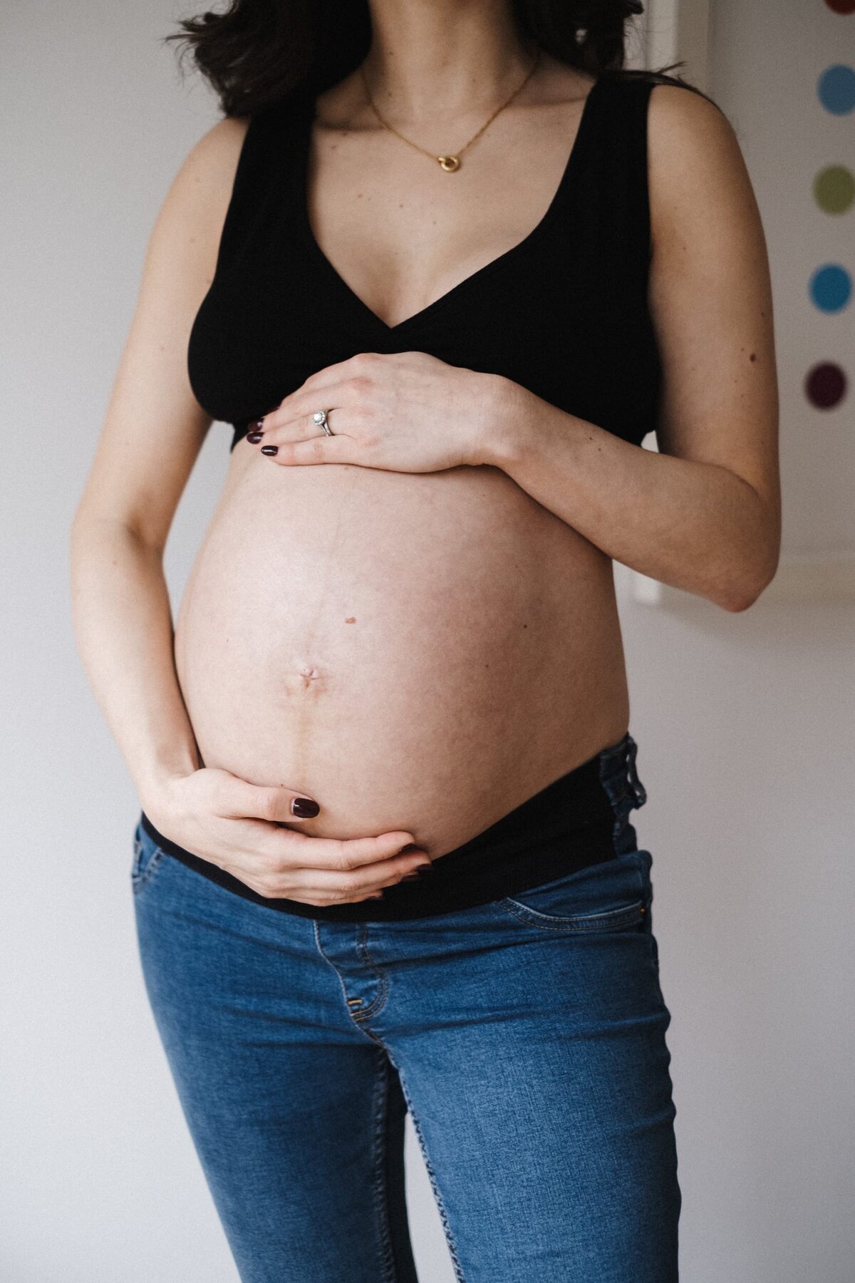 Pregnant woman in black bra and jeans holding her baby bump