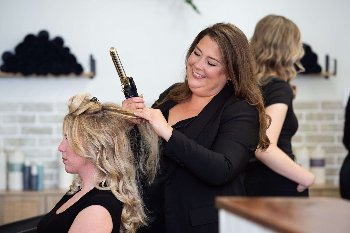 Ottawa branding photography showing a hair stylist dressed in black curling hair on a blonde woman.  Captured on-location at Richardson Hair Design
