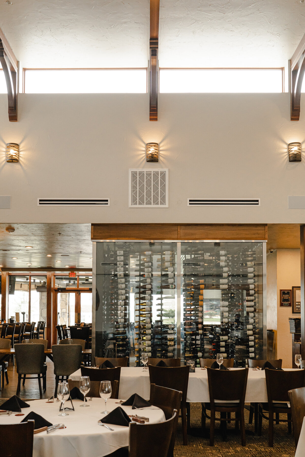 Restaurant interior design with dark wood beams between clerestory windows above wine rack