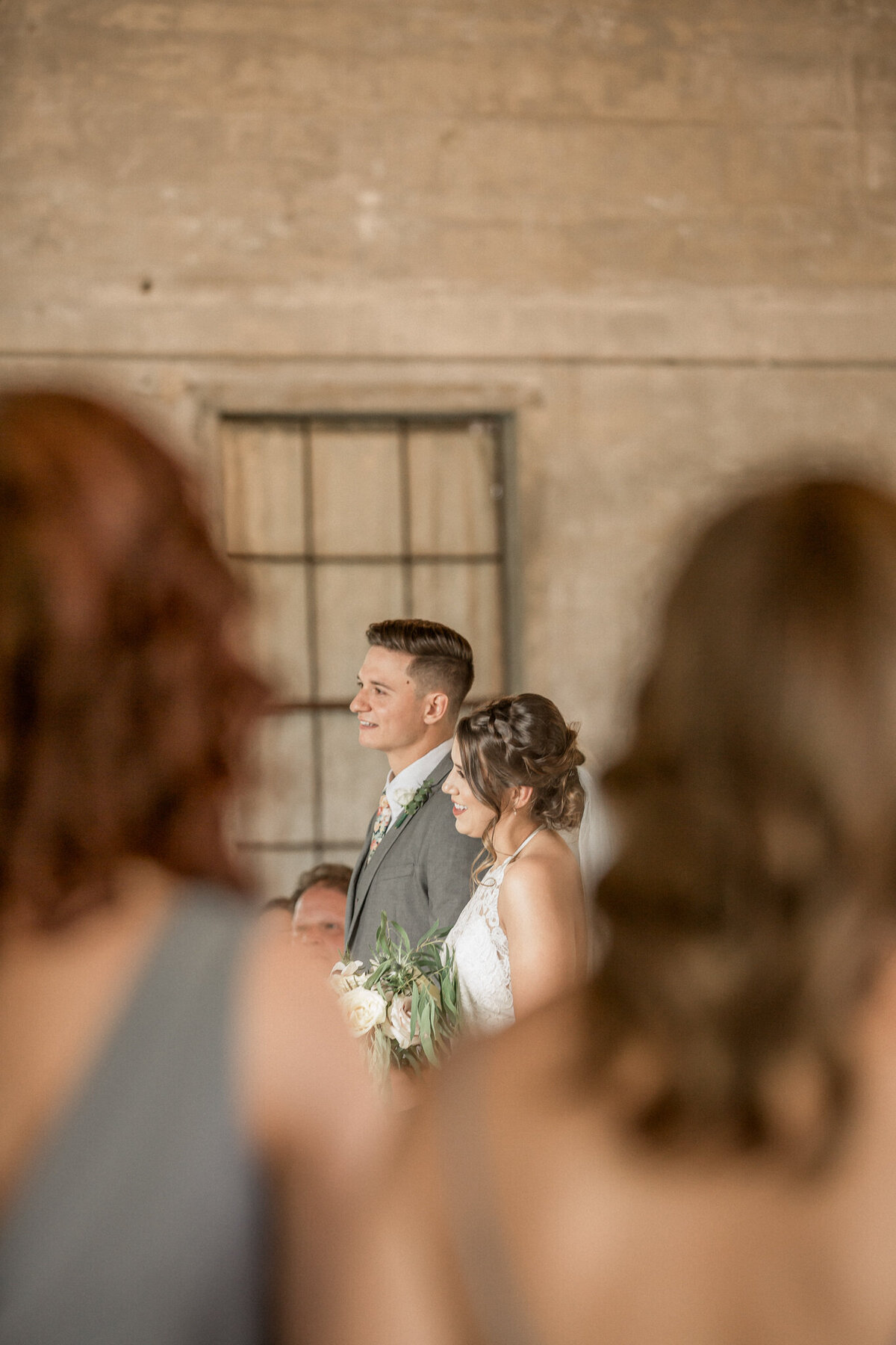 The bride and groom, framed by two bridesmaids, listen attentively to the officiant