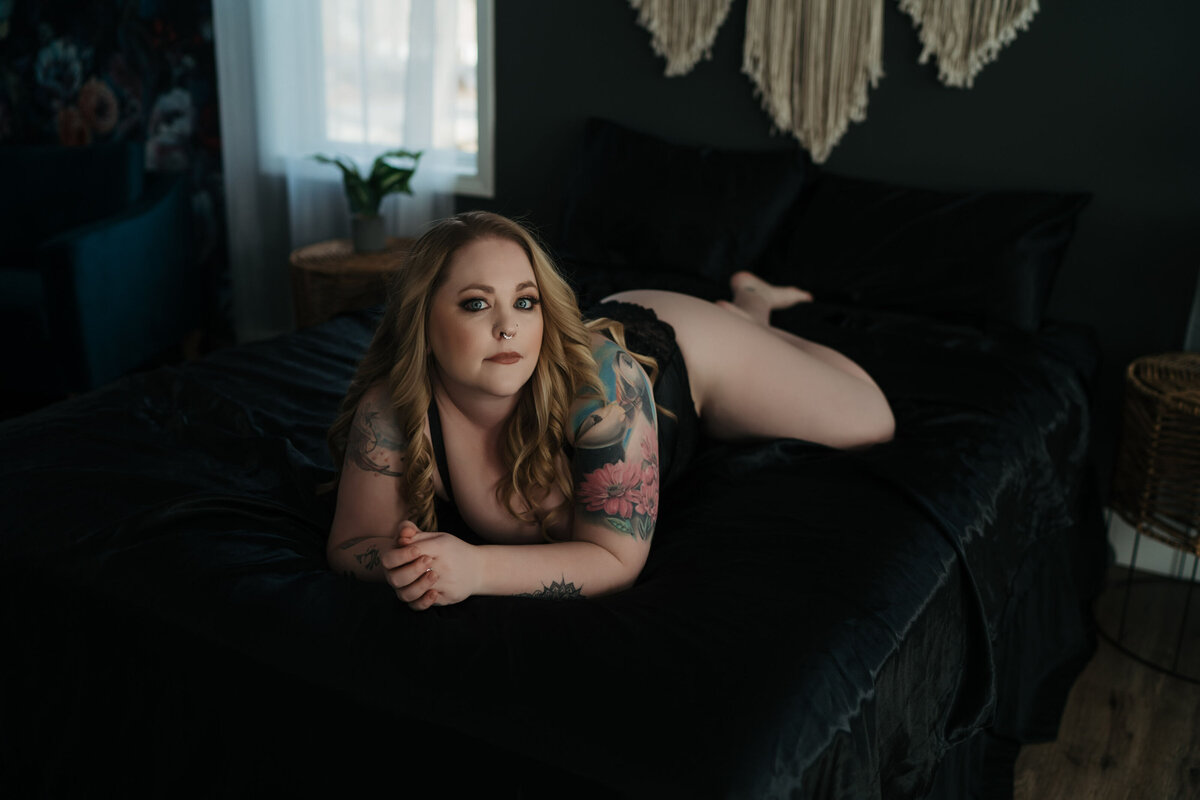 blode woman laying on a black bed in black lingerie as posed by a Boston luxury boudoir photographer