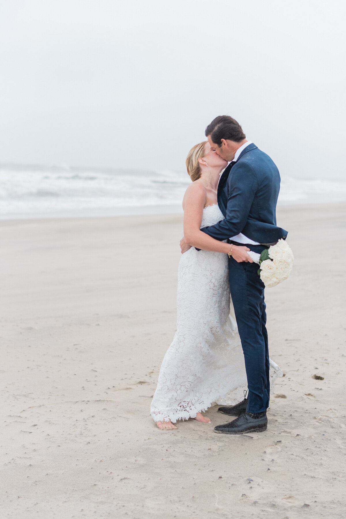 The couple shares a romantic kiss, their bare feet sinking into the damp sand.