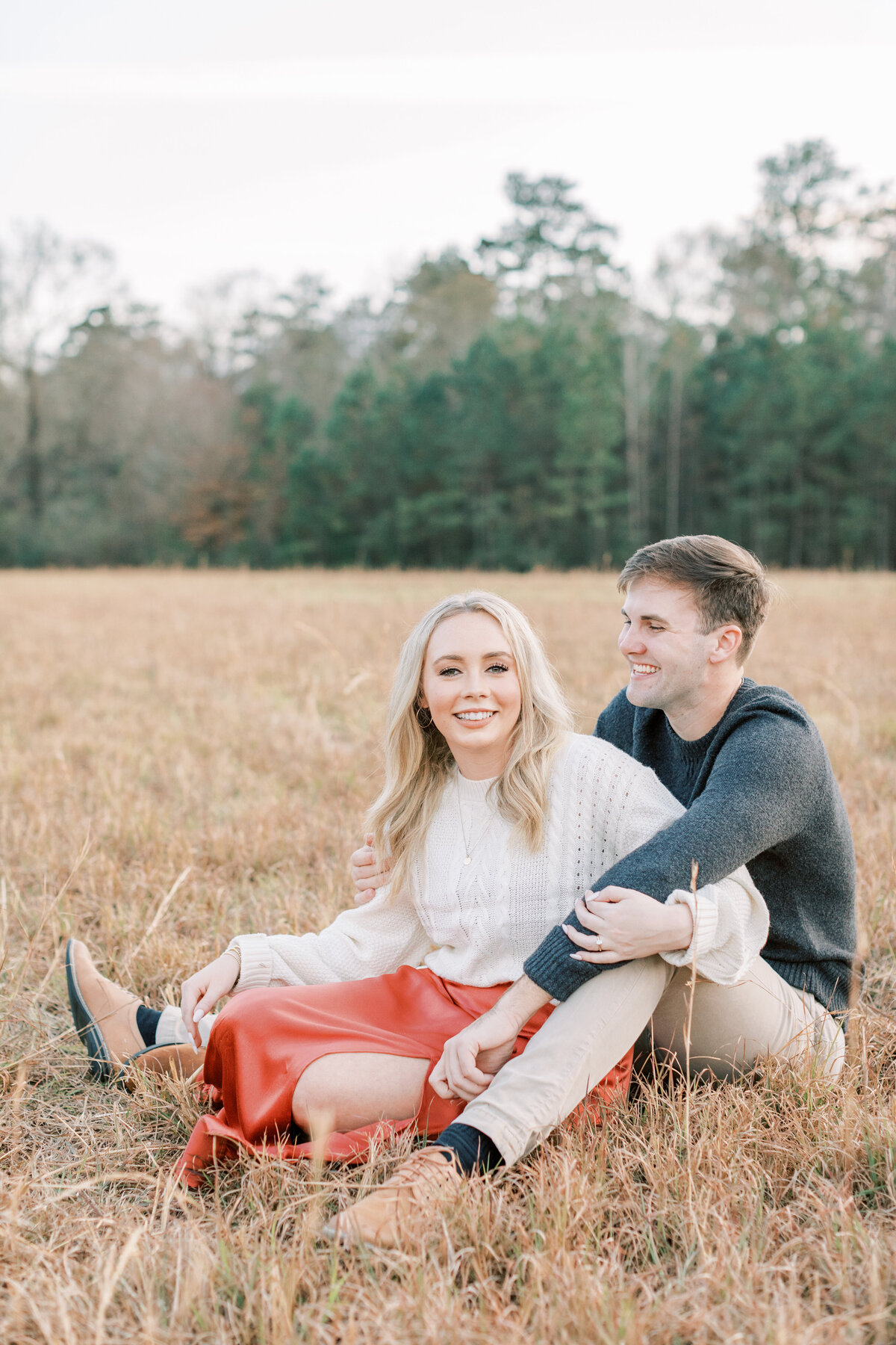 A couple laughs while sitting down in a field.
