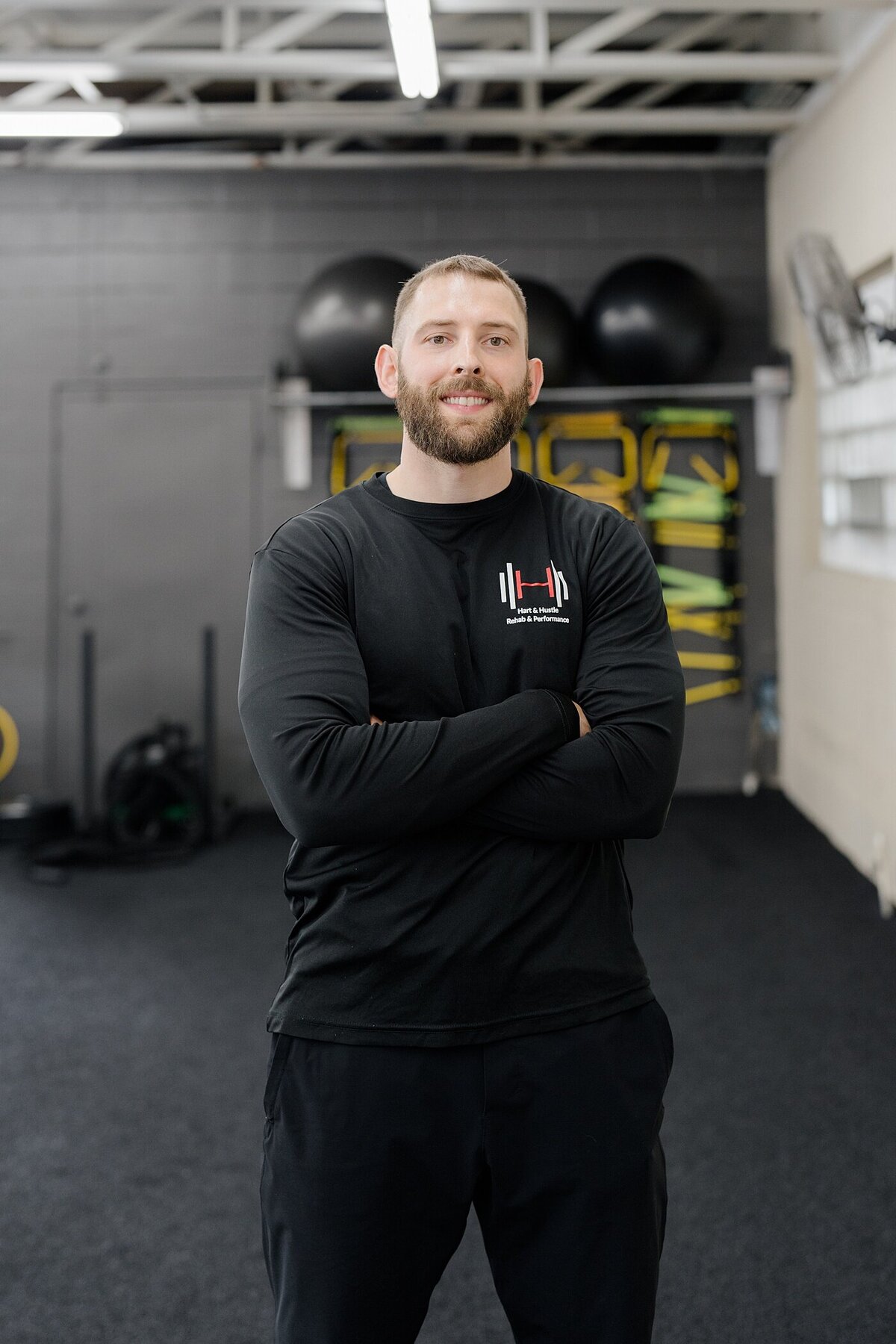 Columbus headshot of training in all black with his arms crossed and smiling in a gym for training photographed by brand photographer in Columbus