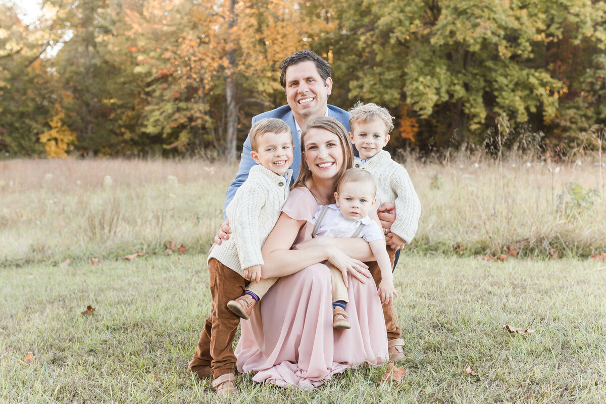 A family kneeling down smiling at the camera outside in the Fall by DC Family Photographer