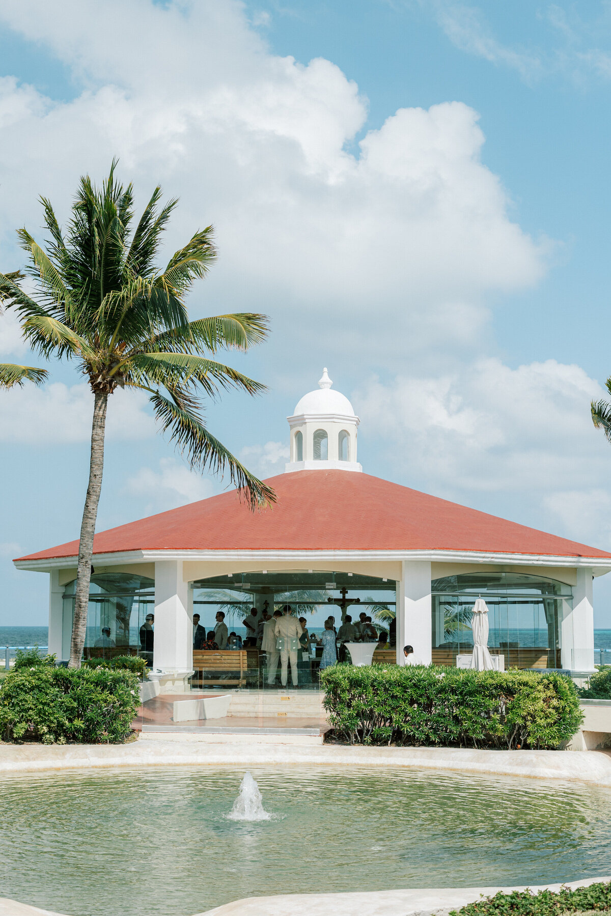 Outdoor wedding chapel in Cancun with red roof, fountain, and palm trees before the ceremony.