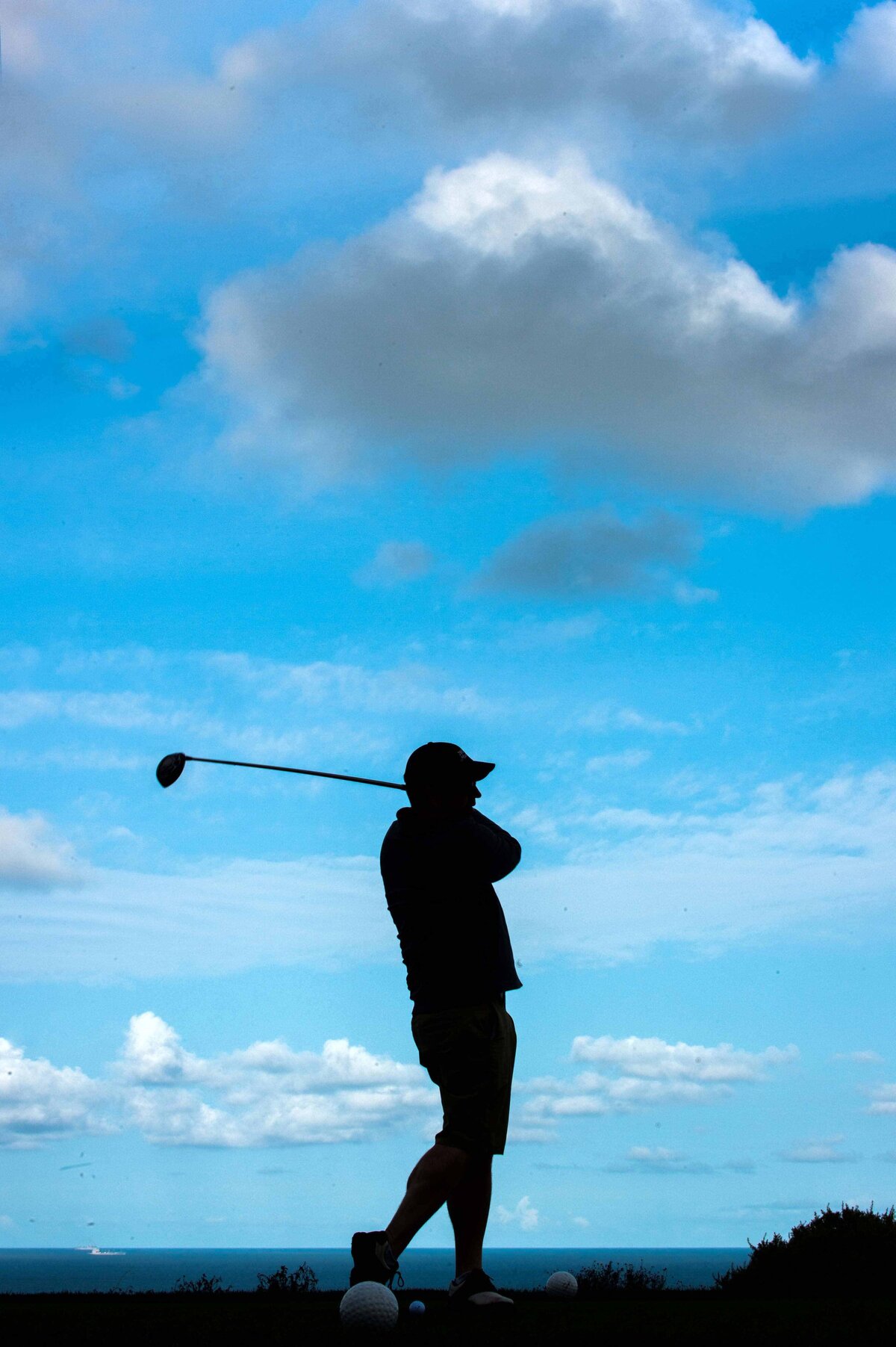 Golfer with club over shoulder silhouetted against sky with golf balls in foreground.