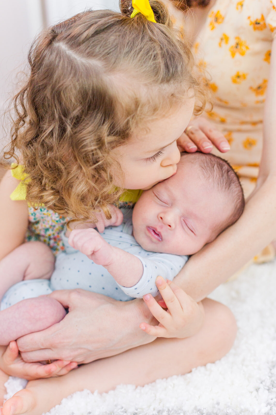 todder sibling kissing newborn baby in mum arms