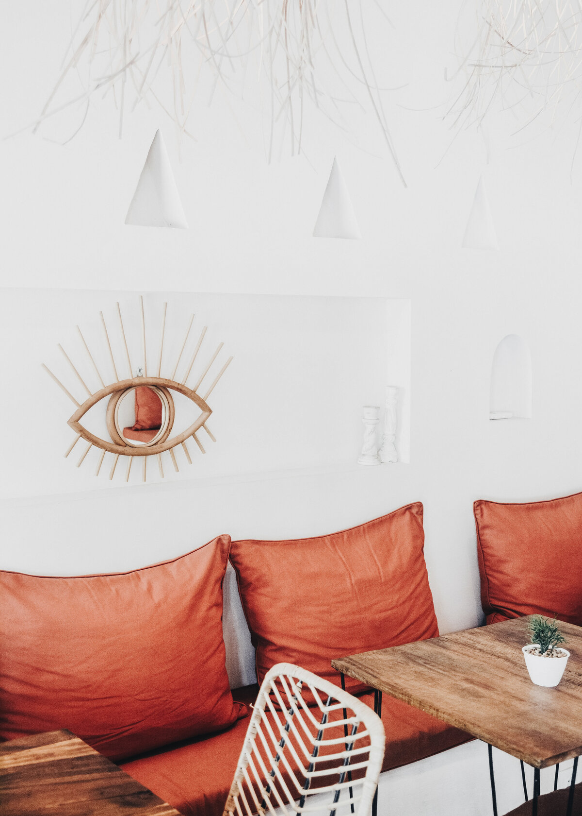 A restaurant has been designed with a boho style with terracotta cushions and an eye shaped mirror.