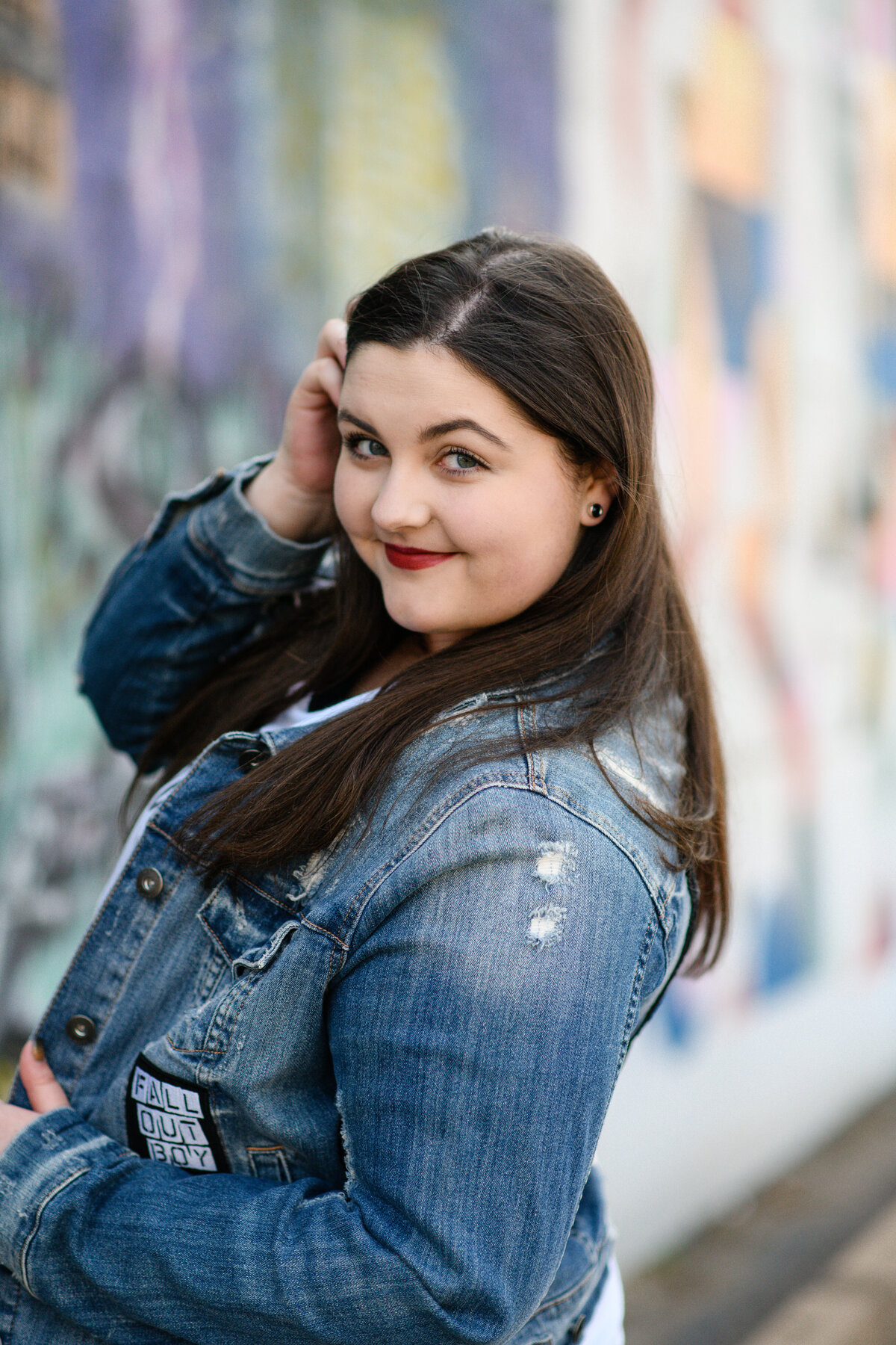 senior picture with senior photo outfit ideas of a girl in a denim coat looking over her shoulder and smiling as she reaches her hand through hair