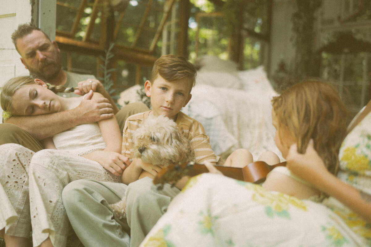 A boy holding his dog in Das Hinterhaus while his sibling strums the guitar. 