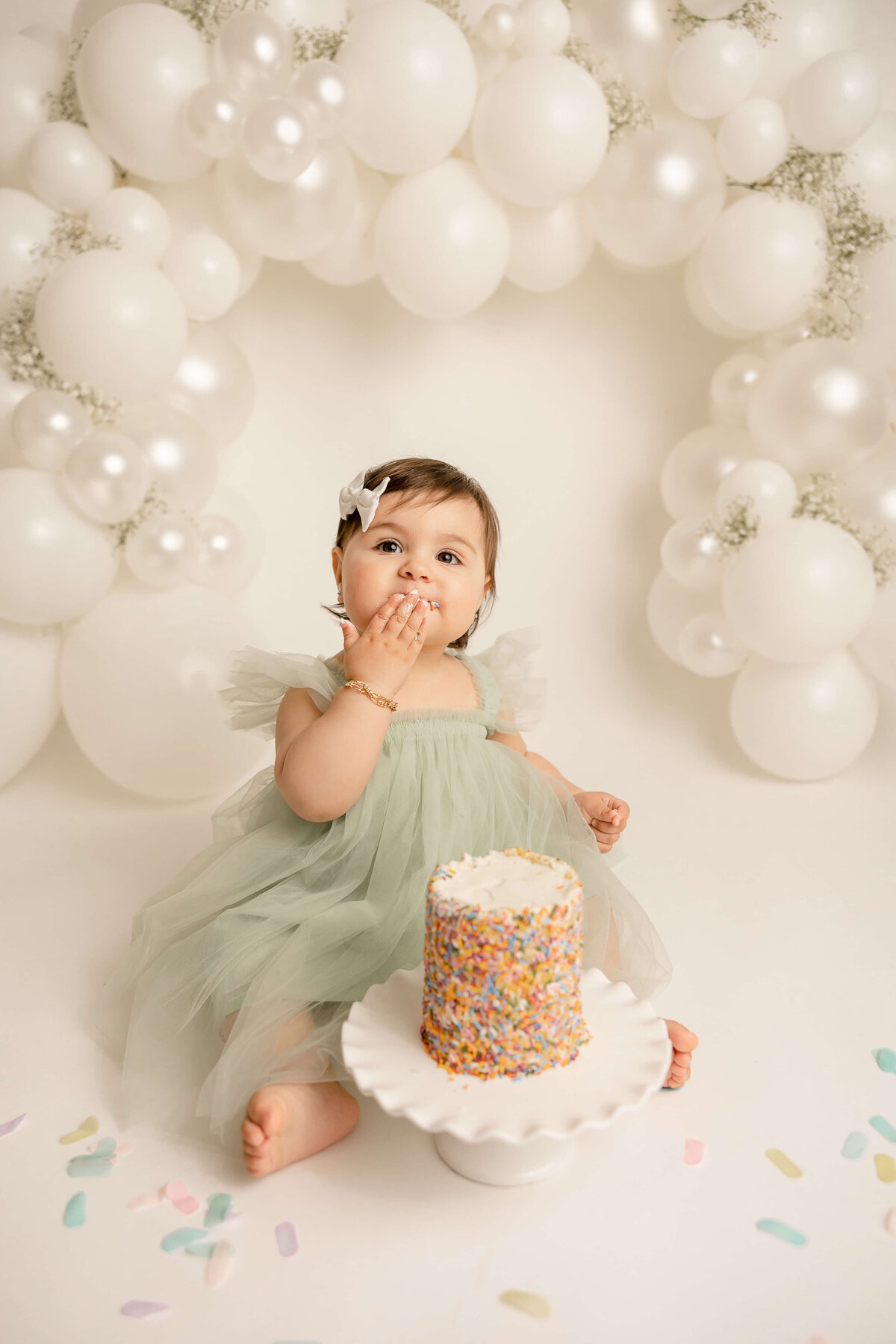 baby girl eating rainbow sprinkle cake in green dress for portland 1st birthday pictures