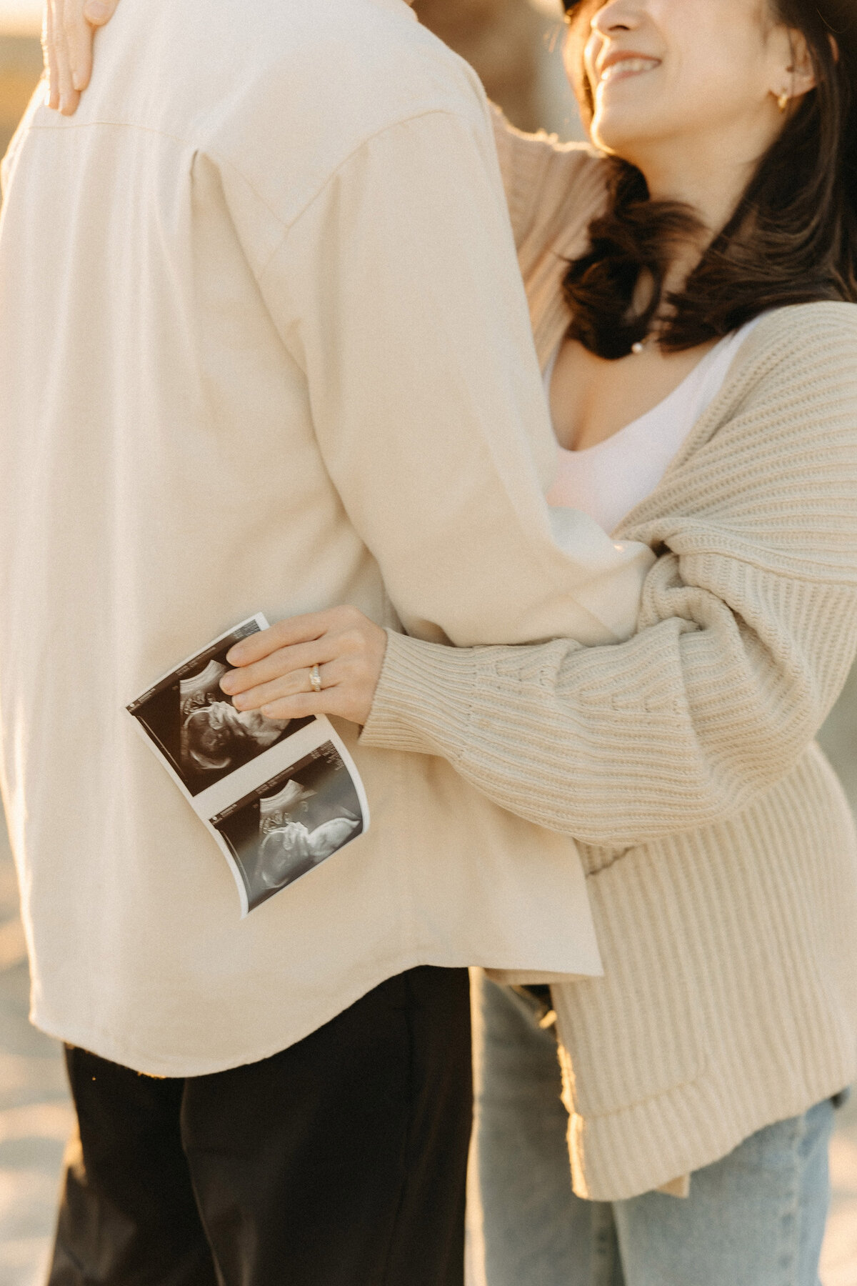 Expecting parents laughing together while holding an ultrasound photo at Coronado Beach maternity session. Captured by San Diego Family Photographer Yuka Schad.