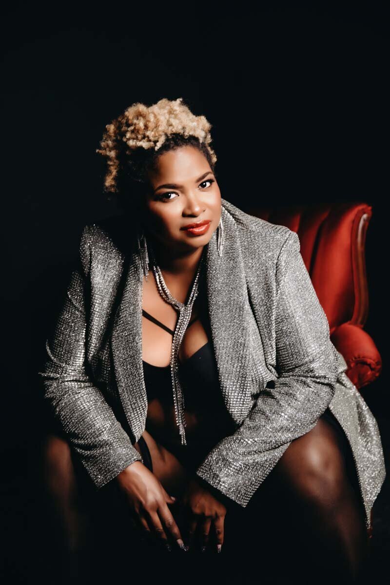 black woman sitting in chair wearing sparkling blazer