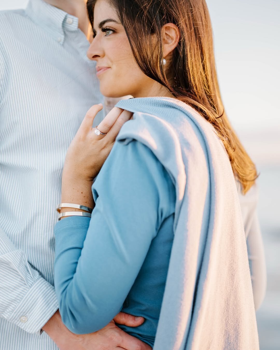 Wedding Photographer RI | A woman in a blue sweater standing closely to a person in a light-colored shirt. She looks relaxed, with soft lighting and a serene background.