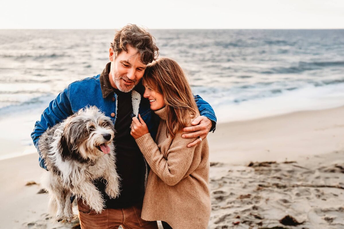 San Diego Family Photographer captures couple hugging while holding dog during beach family photos